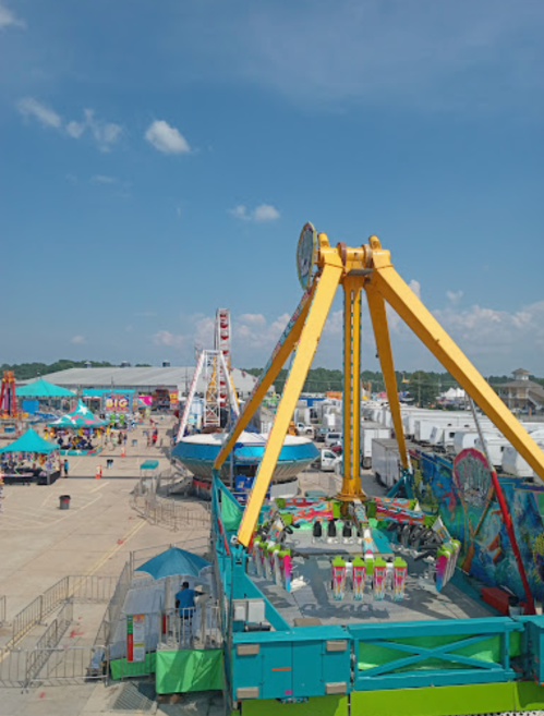 A vibrant carnival scene featuring rides, colorful tents, and a clear blue sky.